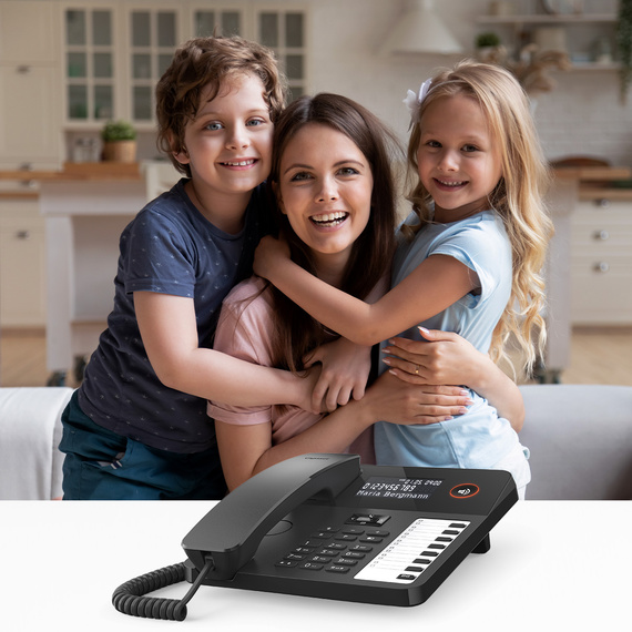 Modern desk phone with display and function keys, in the background a mother and two children.